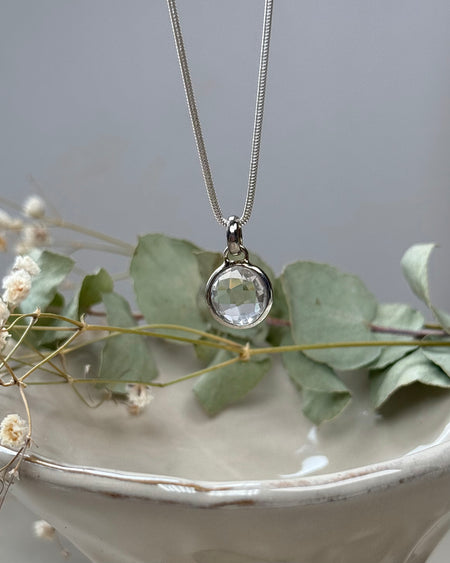 Runder, facettierter Bergkristall-Anhänger, platinbeschichtet, Ø 1 cm, klarer Edelstein mit Glanz, auf hellem Hintergrund