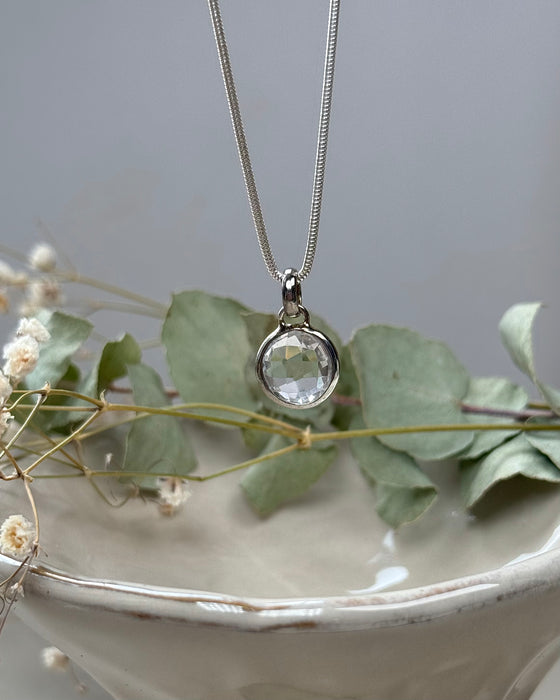Runder, facettierter Bergkristall-Anhänger, platinbeschichtet, Ø 1 cm, klarer Edelstein mit Glanz, auf hellem Hintergrund