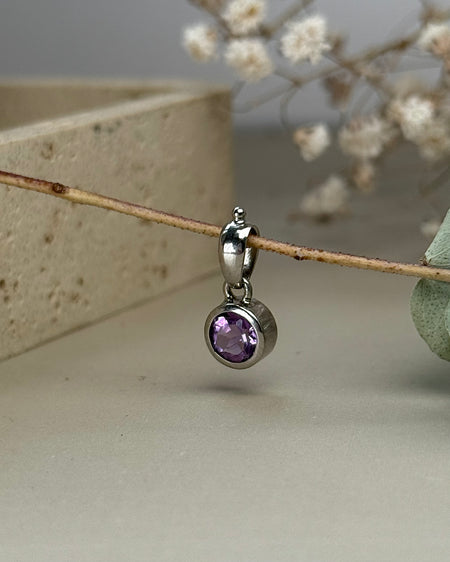 Facettierter Amethyst-Anhänger in 925er Silberfassung, rund, violett leuchtend, Ø 0,8 cm, auf hellem Hintergrund