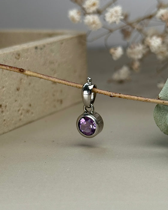 Facettierter Amethyst-Anhänger in 925er Silberfassung, rund, violett leuchtend, Ø 0,8 cm, auf hellem Hintergrund
