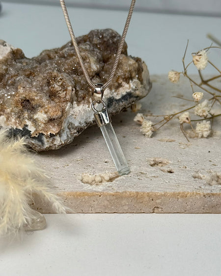 Aquamarinanhänger 2,8 cm, transparenter Kristall mit Silberfassung, vor zarten Trockenblumen.