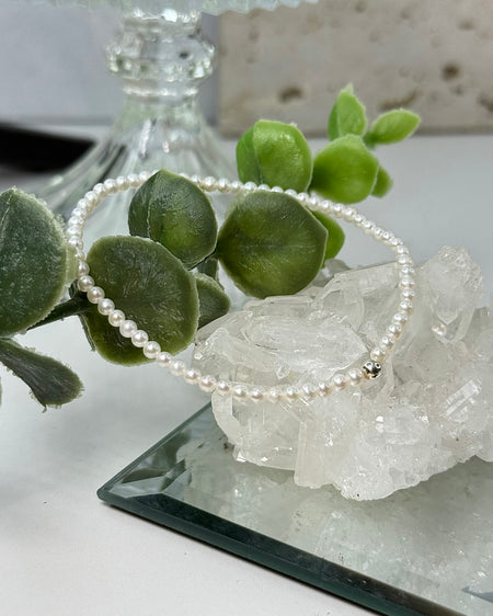 Zartes Süßwasserperlenarmband mit 3-mm-Perlen und einer 925er Silberperle auf hellem Hintergrund.