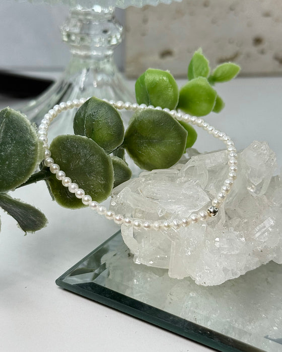 Zartes Süßwasserperlenarmband mit 3-mm-Perlen und einer 925er Silberperle auf hellem Hintergrund.