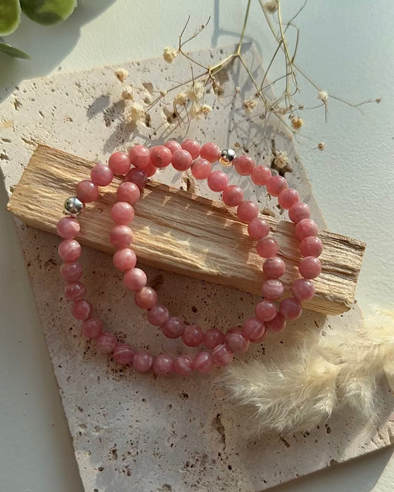 Nahaufnahme eines roséfarbenen Rhodochrosit-Armbands mit gemaserten Rundperlen und Silberakzent.