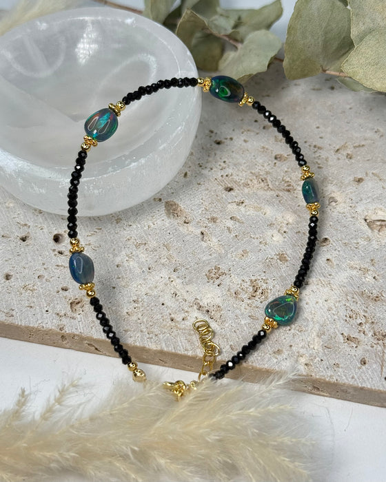Feines Opal-Armband mit schwarzem Opal, Spinell und vergoldeten 925er Silberelementen auf hellem Hintergrund.