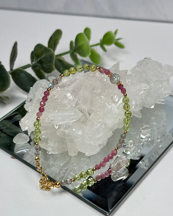 Armband aus Labradorit, rotem Turmalin und Peridot mit vergoldeten Zwischenelementen, 17–22 cm, auf hellem Hintergrund.