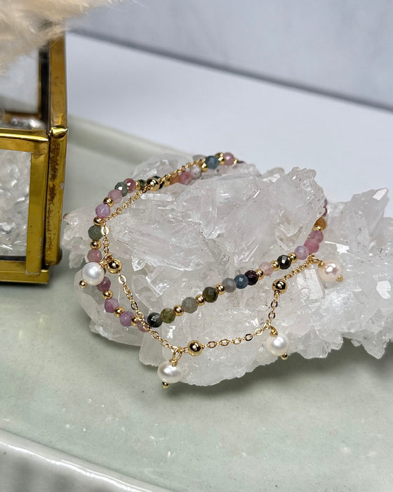 Doppelarmband aus bunten Turmalinperlen mit vergoldeter 925er Silberperle und zweitem vergoldeten Armband mit Süßwasserperle, auf hellem Hintergrund.