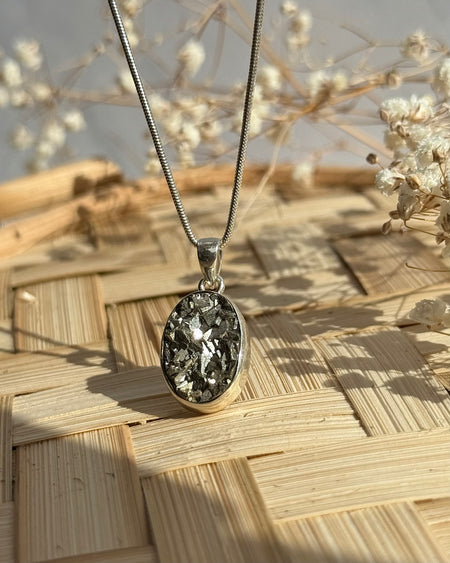 Ovaler Pyrit-Anhänger mit roher, glitzernder Oberfläche, eingefasst in 925er Silber, Naturstein-Schmuck auf Bambusuntergrund.